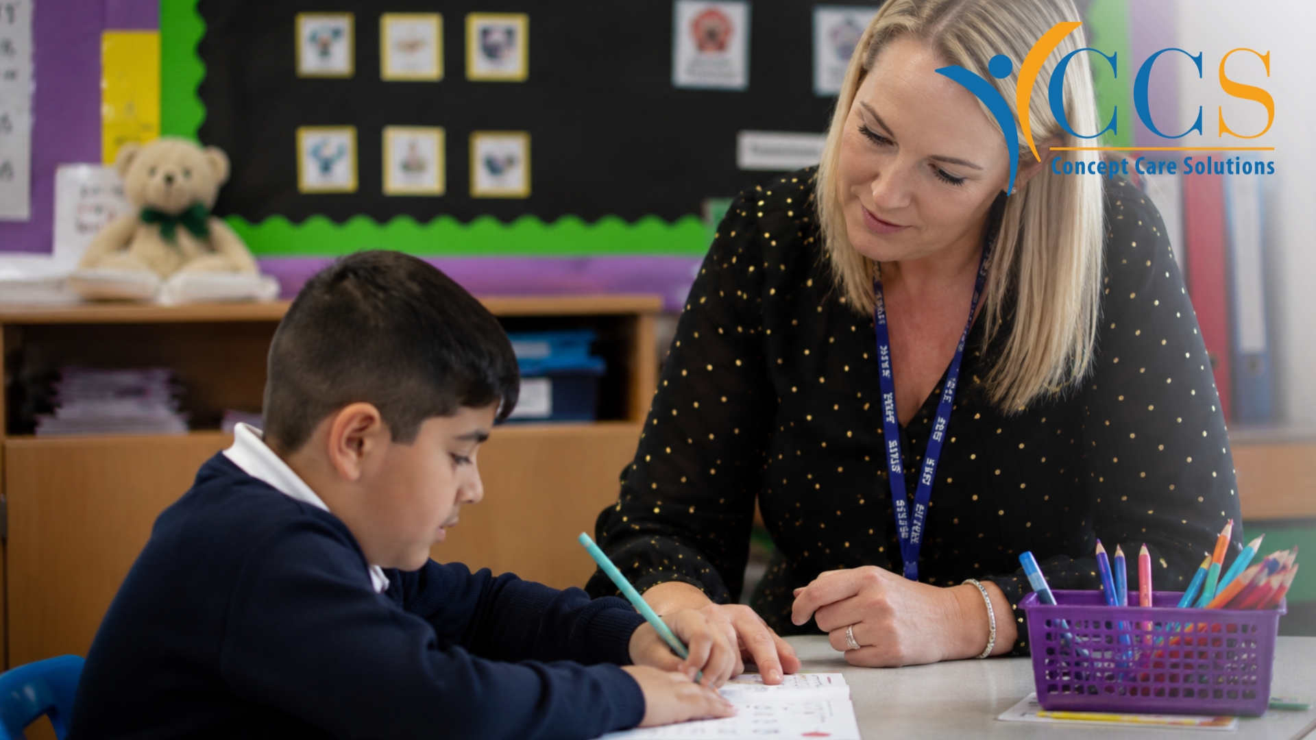 SEN teacher supporting a pupil during a one-to-one lesson in a UK primary school classroom.